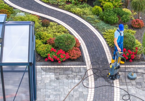 Caucasian Man in His 40s Cleaning His Backyard Garden Paths Using Pressure Washer Aerial View