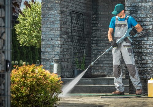 Driveway Pressure Washing. Caucasian Worker Cleaning Area in Front of the House.